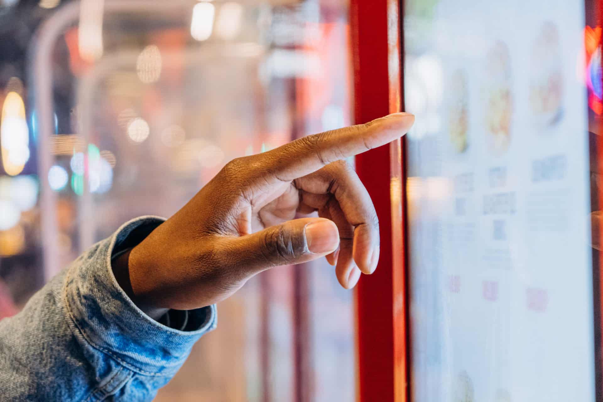 A close-up African finger selects a burger on an electronic touch screen at a self-service checkout at a fast food restaurant