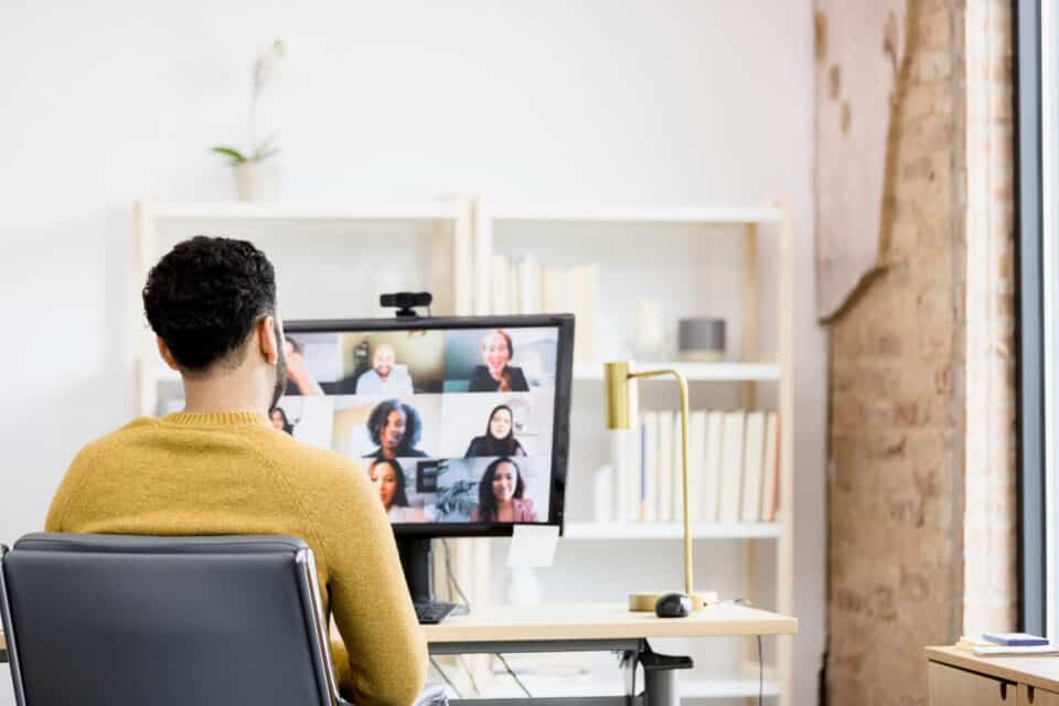 An over-the-shoulder view of an unrecognizable man as he uses his desktop PC for a meeting with diverse co-workers.