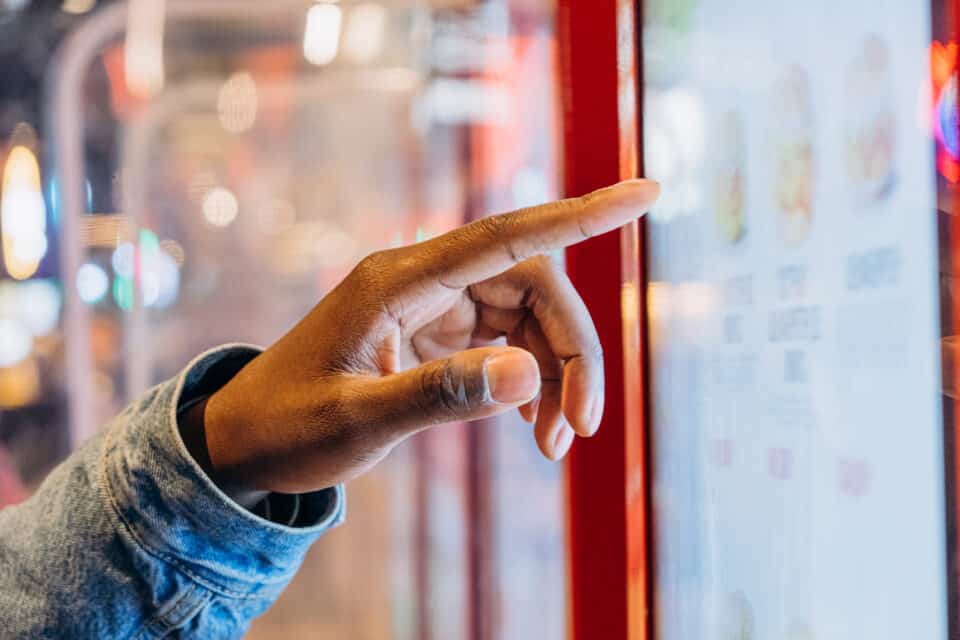 A close-up African finger selects a burger on an electronic touch screen at a self-service checkout at a fast food restaurant