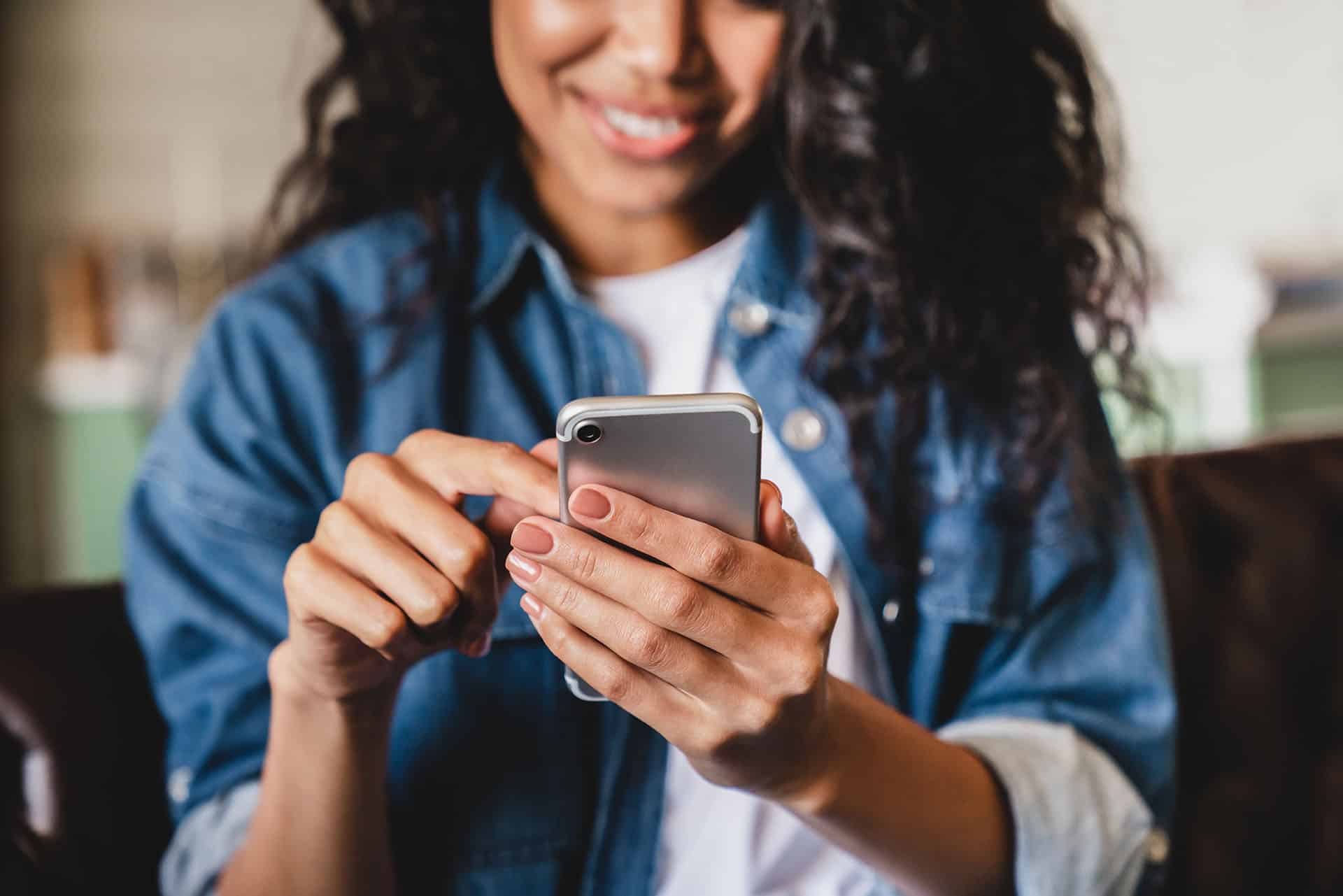 The Case for Cloud Communications 2 Cropped shot of an african-american young woman using smart phone at home.Smiling african american woman using smartphone at home, messaging or browsing social networks while relaxing on couch